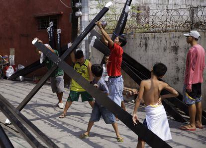 Niños filipinos con cruces de madera, mientras un hombre pinta con spray. Su pueblo se prepara para los rituales en la provincia de Pampanga, en el norte de Filipinas, el 10 de abril de 2017.