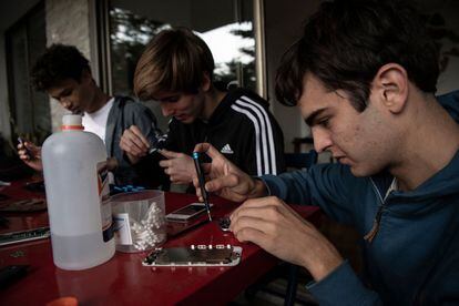 Con lupas, pequeños desarmadores y tornillos, el joven chileno Tiberio Malaiu (derecha) repara teléfonos móviles en desuso que recolectó en una campaña que inició en medio de la pandemia.