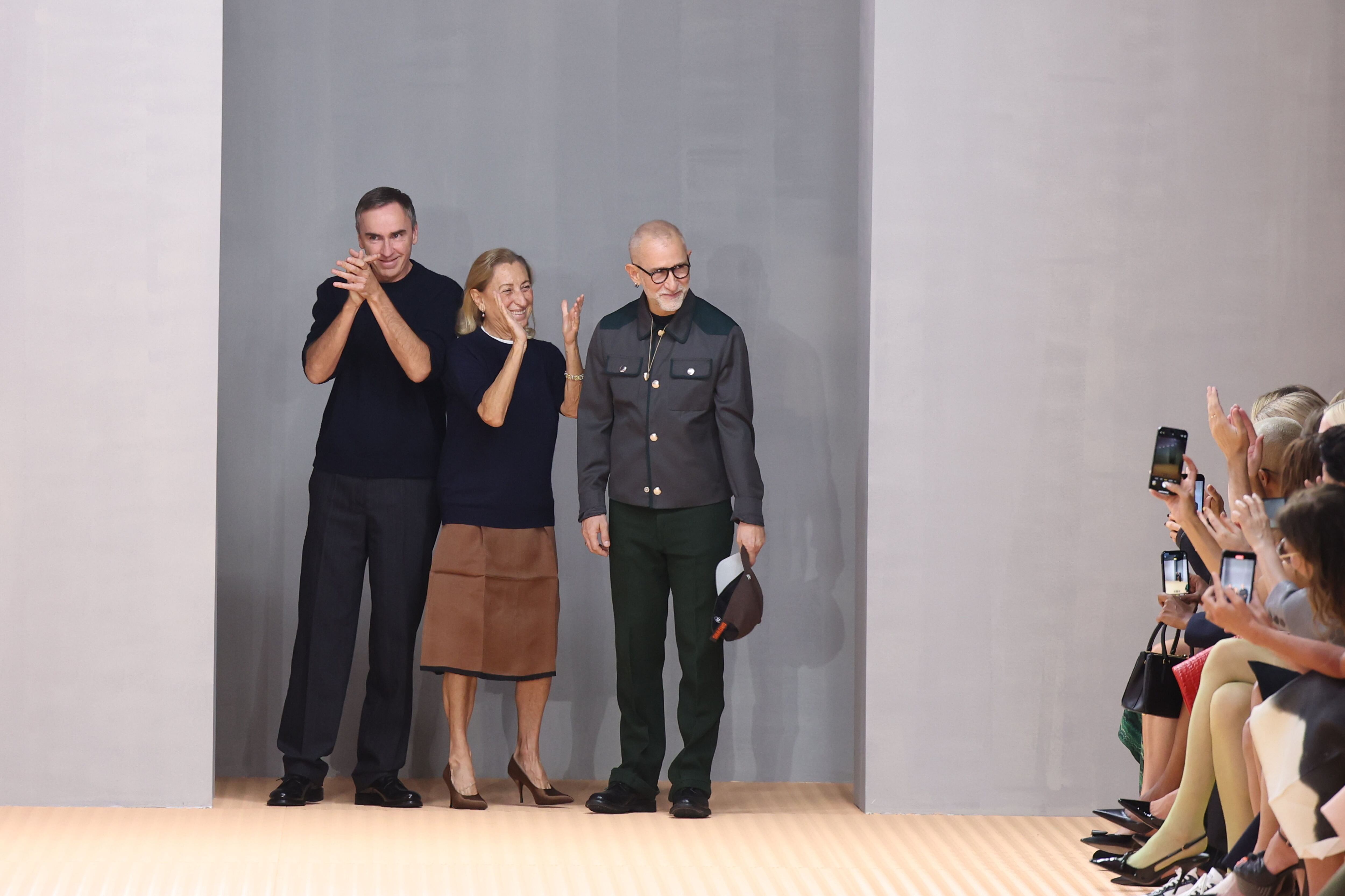 De izquierda a derecha, Raf Simons, Miuccia Prada y Fabio Zambernardi saludan en la pasarela tras el desfile de Prada en la semana de la moda de Milán.