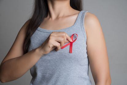 Closeup woman hand holding red ribbon HIV, world AIDS day awareness ribbon. Healthcare and medicine concept.