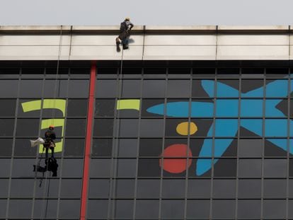 Varios operarios quitan el logotipo de Bankia para incorporar, sobre las ventanas más altas del edificio, la imagen de CaixaBank.