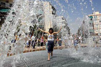 Una niña combate el calor al pasar bajo los surtidores de la fuente de la renovada Plaza de Manila de Alicante.