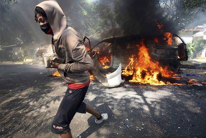 Un partidario sandinista acarrea una piedra delante de un coche en llamas durante los disturbios.