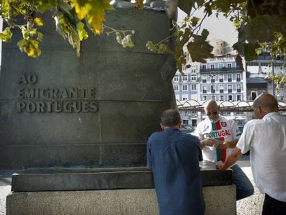 Un grupo de taxistas juegan a las cartas al lado de la estatua dedicada al emigrante portugués.