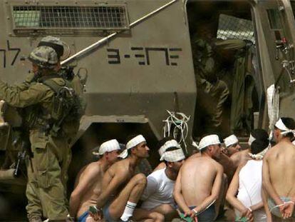 Varios presos palestinos en ropa interior esperan maniatados junto a un blindado del Ejército de Israel.