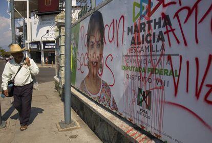 Un hombre pasa al lado de un cartel grafiteado del PRI en Oaxaca.