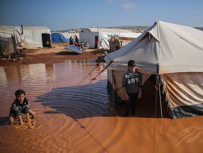 Dos niños sirios son fotografiados junto a su casa, una tienda de campaña, ahora inundada debido a las inundaciones a causa de las fuertes lluvias que cayeron sobre el campo de refugiados de Ma'arrat al-Nu'man, en Siria, el 17 de diciembre de 2020.