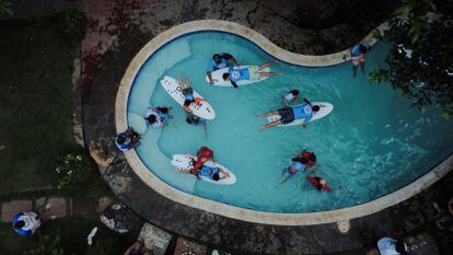 Acompañados por instructores, un grupo de niños recibe sus primeras clases de surf dentro de una piscina.