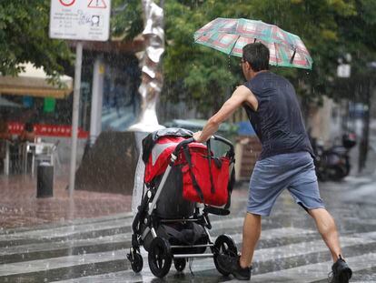 Un padre (de espaldas) empuja un carrito de bebé bajo la lluvia en Terrassa (Barcelona), en una imagen de archivo.