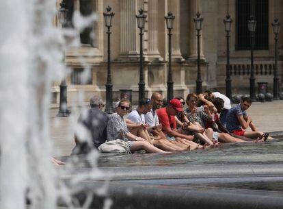 Un grupo de turistas se refrescan los pies en una fuente próxima al museo Louvre de París (Francia), el 21 de junio.
