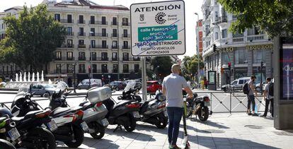 Un usuario de patinete eléctrico pasa junto a un cartel que avisa de la prohibición al paso de los vehículos más contaminantes en la capital, instalado en la glorieta de Bilbao.