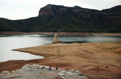 Dos personas caminan alrededor de los restos de la iglesia de Sant Roma de Sau que emerge del embalse de Sau, al norte de Barcelona, el lunes 8 de agosto.