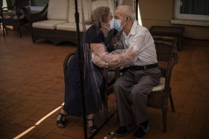 Agustina Cañamero, de 81 años, abraza y besa a su marido Pascual Pérez, de 84, a través de una pantalla de plástico como medida preventiva contra el coronavirus en una residencia de ancianos en Barcelona, el 22 de junio de 2020.