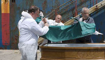 Cuatro hombres portan el cuerpo de un inmigrante fallecido, este martes en el puerto de Catania. 