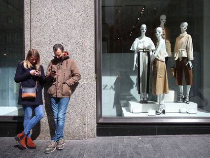 Dos jóvenes usan sus móviles ante una tienda Zara en Madrid.