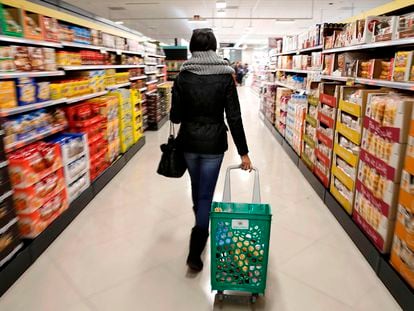 Una mujer carga su carrito de la compra por el pasillo de un supermercado.