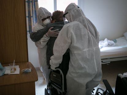 Dos personas ayudan a una mujer mayor a sentarse en una silla de ruedas en una residencia geriátrica de Barcelona, en abril.