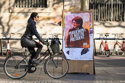 Joven pasa con su bicicleta cerca de un cartel electoral del expresidente Pugidemont en Barcelona.
