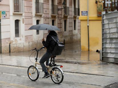 Un ciclista se protege de la lluvia con un paraguas, este jueves en Valencia.