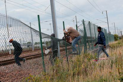 Inigrantes pasan por encima de una valla para entrar en el área del Eurotunnel, en Calais.