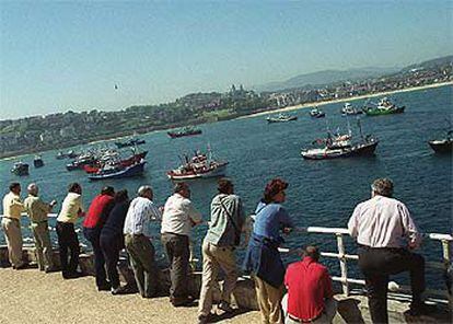 Un grupo de personas observa la concentración de barcos de la flota del Cantábrico en la bahía de La Concha, en San Sebastián.