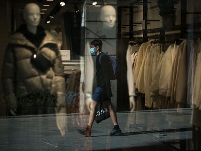 Un joven camina con mascarilla frente al escaparate de una tienda en Barcelona.