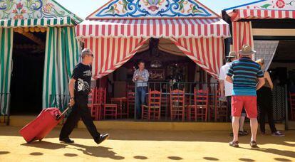 Un visitante, con su equipaje en la Feria de Sevilla mientras un grupo de turistas observa las casetas.