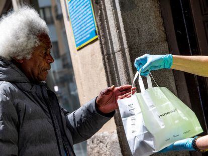 Una voluntaria de Mensajeros de la Paz entrega una bolsa con comida a una persona que ha quedado en situación vulnerable a causa del impacto de la covid-19 en Madrid, en mayo de 2020.