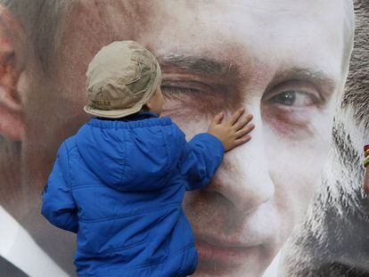 Un niño toca un cartel con la imagen del presidente ruso, Vladimir Putin.