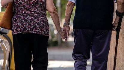 Un hombre y una mujer mayores caminando cogidos de la mano por la calle Caramuel, en el barrio de Puerta del Ángel, Madrid.