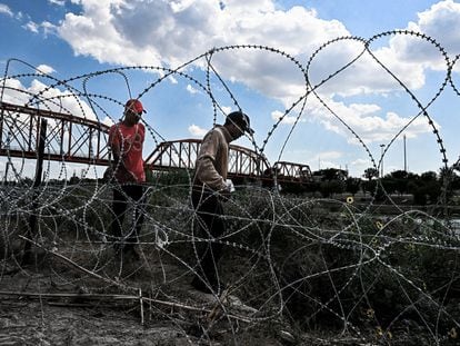 Migrants who illegally crossed the Rio Grande River walk along concertina wire in Eagle Pass, Texas, near the border with Mexico on June 30, 2022. - Every year, tens of thousands of migrants fleeing violence or poverty in Central and South America attempt to cross the border into the United States in pursuit of the American dream. Many never make it. On June 27, around 53 migrants were found dead in and around a truck abandoned in sweltering heat near the Texas city of San Antonio, in one of the worst disasters on the illegal migrant trail. (Photo by CHANDAN KHANNA / AFP)