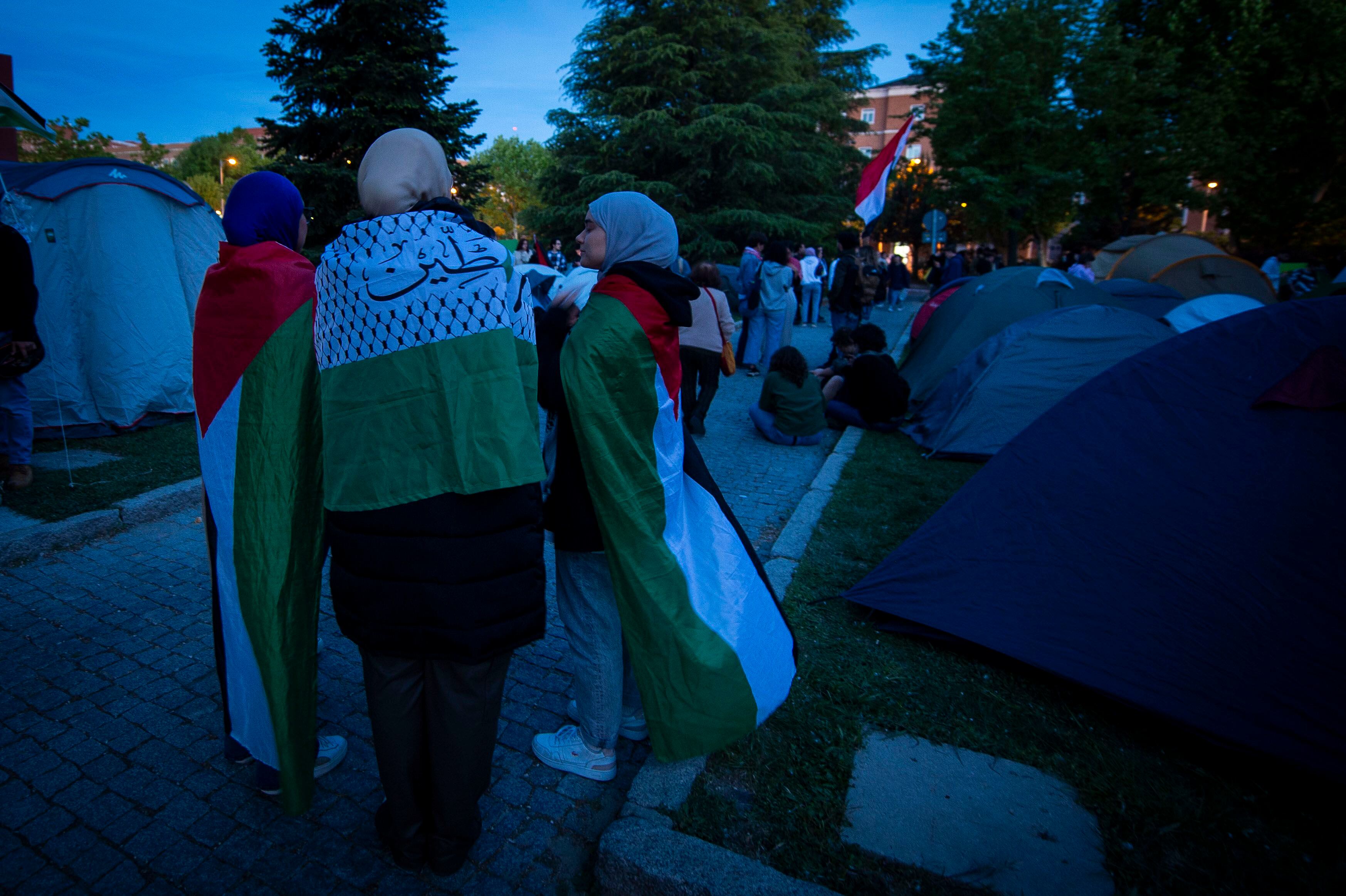 Tres mujeres arropadas con las banderas de Palestina en el campamento estudiantil de Ciudad Universitaria.
