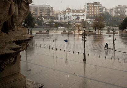 Un solitario ciclista pasea bajo la lluvia frente al palacio de San Telmo en Sevilla.