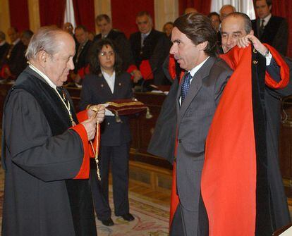 Landelino Lavilla (derecha) y José Joaquín Puig de la Bellacasa (izquierda), los dos miembros del Consejo de Estado elegidos por el expresidente del Gobierno para actuar como padrinos en la ceremonia en la que juró su cargo como miembro nato con carácter vitalicio de la institución. Le entregan la toga y la insignia del Consejo, ambos elementos formales de la toma de posesión. Menos de un año más tarde Aznar abandonaba el Consejo de Estado al fichar como consejero de News Corp, la multinacional de Rupert Murdoch. Más tarde se sabría que desde mediados de 2004 cobraba 10.000 euros al mes por asesorar a Murdoch.