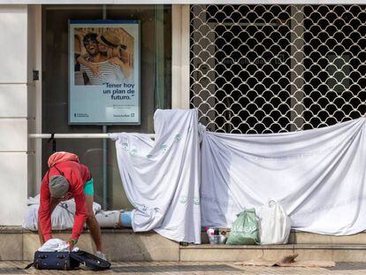 Una persona sin hogar recoge sus pertenencias tras haber pasado la noche en la puerta de una entidad bancaria en pleno centro de Sevilla. 