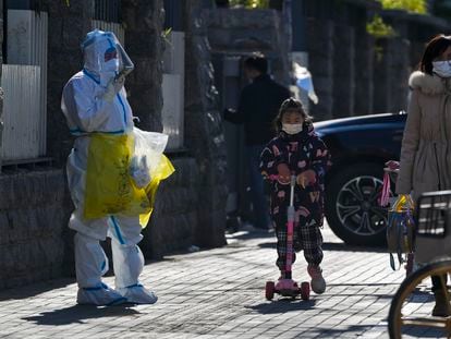 Una niña con mascarilla pasa junto a un trabajador que recoge muestra de control de la covid, este jueves en Pekín.