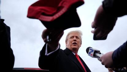 El expresidente Donald Trump entrega una gorra a un seguidor mientras habla los medios durante la campaña en New Hampshire, el 23 de enero de 2024.