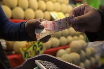 A customer pays for fruit with a 100-peso bill at a stand in Central de Abastos, Mexico City.
