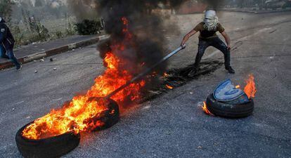 Un manifestante palestino usa un palo para mover unas ruedas ardiendo durante los enfrentamientos con las fuerzas de seguridad israelíes cerca del puesto de control de Qalandia, en Cisjordania.