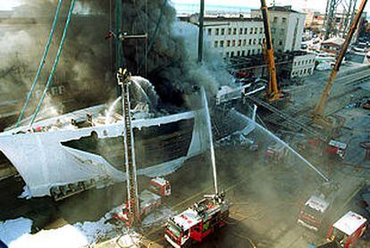 Los bomberos trabajan en la extinción del incendio de un velero en el puerto de Barcelona.