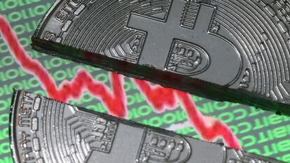 Un bitcoin roto, colocado en un monitor que muestra un gráfico de acciones y códigos binarios.