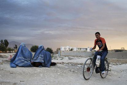 Un joven pasa en su bicicleta junto a dos mujeres ataviadas con burka en el norte de Kabul.