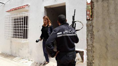 Un agente tunecino junto a una periodista que abandona la casa en la que dos yihadistas han muerto este mi&eacute;rcoles. 