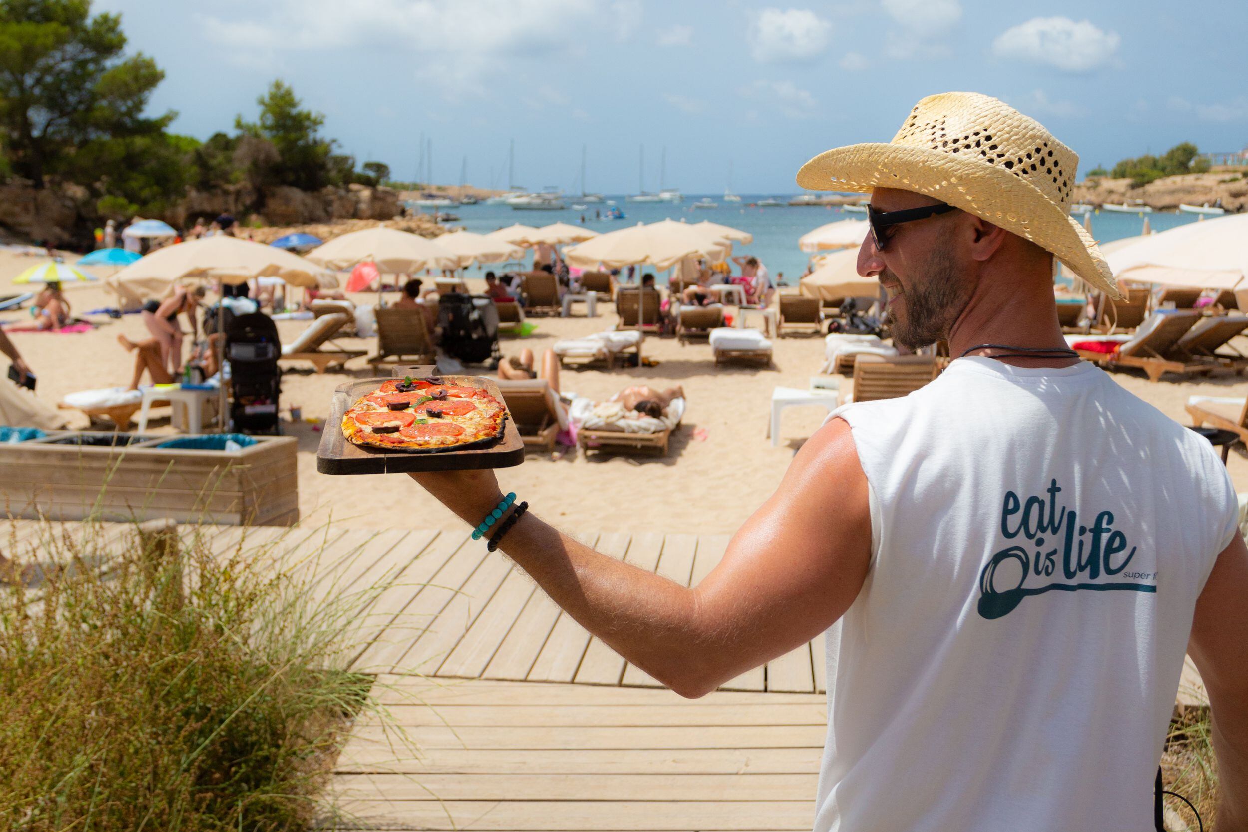 Un camarero del chiringuito Alma Eat Is Life (Ibiza) acerca una pizza a las sombrillas.