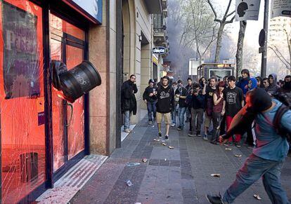 Un joven radical arroja una papelera contra las puertas de una oficina bancaria de Barcelona.