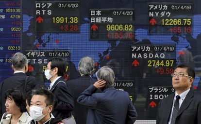 Ejecutivos japoneses caminan frente a una pantalla que muestra los valores de la Bolsa de Tokio.