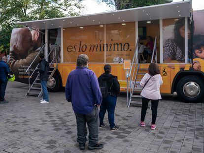 Varias personas esperan para entrar en un autobús que informa sobre el ingreso mínimo vital, en 2022 en Parla (Madrid).