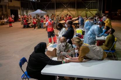 Una trabajadora del Gobierno da la bienvenida a una familia evacuada. En segundo plano, los sanitarios realizan pruebas PCR a los que han viajado en el avión, este jueves en Torrejón de Ardoz.