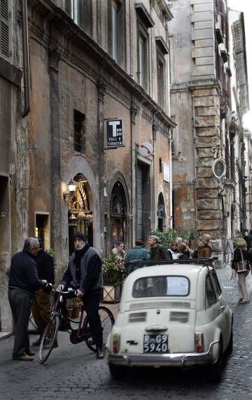 Un ciclista y un coche pequeño en una calle adoquinada de Roma.