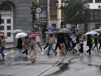 Varias personas cruzan un paseo de peatones protegidas con paraguas, junto al Teatro Campoamor de Oviedo, este sábado.